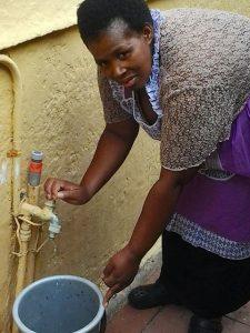 Queenie Magubane, de 38 años y oriunda de la municipalidad de Khayelitsha en Ciudad del Cabo, usa un balde para recolectar agua que gotea constantemente del grifo exterior de su casa. Es uno de los miles de grifos con fugas en Sudáfrica. Crédito: Melany Bendix/IPS
